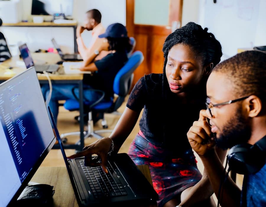 Two professionals collaborating — a woman pointing at a computer screen while offering suggestions to her colleague